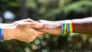 Zwei Menschen mit Regenbogenarmbändern halten sich an den Händen © Colourbox Foto: #311807