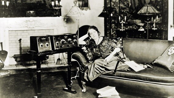 Schwarz-Weiss-Aufnahme einer Frau mit Kophörern auf einem Sofa, die Radio hört,1923. © picture alliance Foto: Courtesy Everett Collection