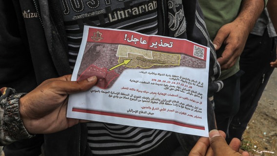 Palästinenser halten ein Flugblatt in der Hand, das von einem Militärflugzeug der israelischen Armee über dem Osten der Stadt Rafah abgeworfen wurde und sie auffordert, die Stadt zu evakuieren. © Abed Rahim Khatib/dpa 