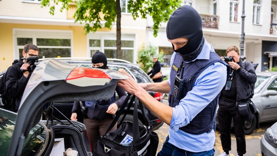 Ein Polizist stellt bei einer Hausdurchsuchung in Berlin-Kreuzberg eine Tasche in ein Fahrzeug. © Christoph Soeder/dpa Foto: Christoph Soeder