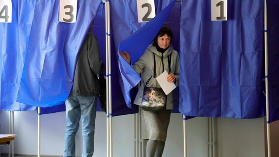 Eine Frau hält ihren Stimmzettel in der Hand, als sie eine Wahlkabine während des Scheinreferendums in einem Wahllokal in der von den von Russland unterstützten Separatisten kontrollierten Volksrepublik Donezk verlässt. © picture alliance/dpa/AP | Uncredited Foto: ---