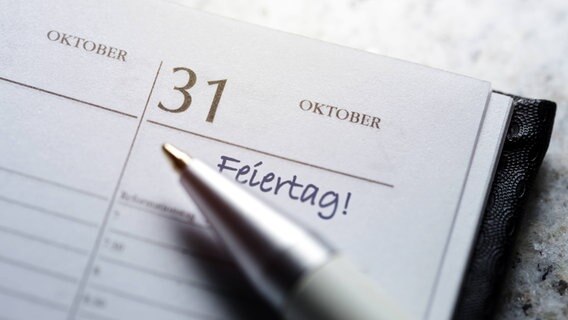 Ein Stift liegt auf einem Kalender, der am 31. Oktober aufgeschlagen ist - und an dem das Wort "Feiertag" notiert wurde. © picture alliance/chromorange Foto: Christian Ohde