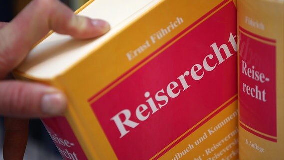 Eine Hand greift eine Gesetzbuch zum Reiserecht aus dem Regal © picture alliance/Oliver Berg/dpa Foto: Oliver Berg