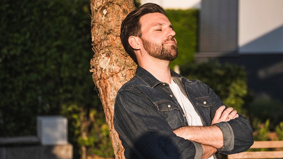 Ein Mann steht an einem Baum in der Sonne und schließt die Augen. © picture alliance / Westnend61 Foto: Uwe Umstätter