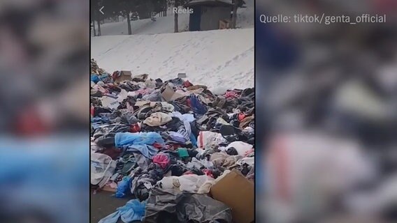 Kleider und Müllsäcke voll mit Kleidern am Straßenrand, dahinter Schnee. © NDR 