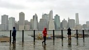 Mehrere Menschen stehen im Regen und Sturm und blicken auf Manhattan. © dpa-Bildfunk Foto: Justin Lane