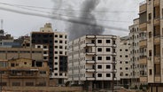 Während eines Einsatzes der syrischen Sicherheitskräfte in der Stadt Scharaja steigt Rauch hinter einem Gebäude auf. © AP/dpa Foto: Omar Albam