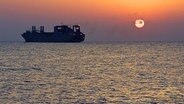 Ein Frachter fährt durch das Mittelmeer. Im Hintergrund geht die Sonne unter. © dpa Foto: Hilke Segbers