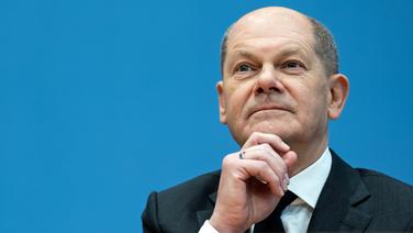 Olaf Scholz (SPD), designierter Bundeskanzler, sitzt in der Bundespressekonferenz. Er hat die Hand am Kinn und wirkt nachdenklich. © dpa-Bildfunk 