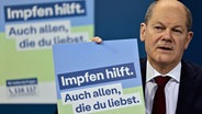 Bundeskanzler Olaf Scholz (SPD) präsentiert ein Plakat für eine neue Impfkampagne während einer Pressekonferenz nach einem Treffen im Kanzleramt (24.01.2022). © dpa-Bildfunk Foto: Hannibal Hanschke/POOL AP/dpa
