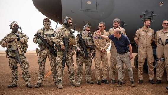 Bundeskanzler Olaf Scholz steht in Tillia in Niger vor einem Flugzeug neben Bundeswehrsoldaten. © dpa Bildfunk Foto: Michael Kappeler