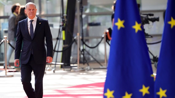 Bundeskanzler Olaf Scholz ist beim EU-Gipfel in Brüssel neben EU-Flaggen zu sehen. © Olivier Matthys/AP Pool/dpa 
