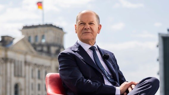 Bundeskanzler Olaf Scholz sitzt vor einem Interview in einem Sessel, im Hintergrund das Reichstagsgebäude. © Christoph Soeder 