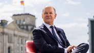 Bundeskanzler Olaf Scholz sitzt vor einem Interview in einem Sessel, im Hintergrund das Reichstagsgebäude. © Christoph Soeder 