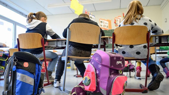 Schulranzen stehen in einer Grundschule. Kinder sitzen an ihren Tischen. © dpa picture alliance Foto: Sebastian Gollnow