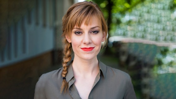 Moderatorin Eva Schulz steht vor einem unscharfen Hintergrund und lächelt in die Kamera. © NN 