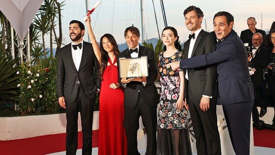 Regisseur Sean Baker (3.v.l.) und mehrere Schauspielerinnen und Schauspieler posieren mit der Goldenen Palme für den Film "Anora" nach der Preisverleihung der 77. Internationalen Filmfestspiele in Cannes. © dpa-Bildfunk/XinHua Foto: Gao Jing