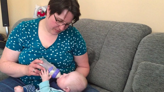 Rebecca Seffrin hält ihr Baby Bennet auf dem Schoß und gibt ihm eine Flasche mit Milch. © NDR Foto: Niklas Schenck