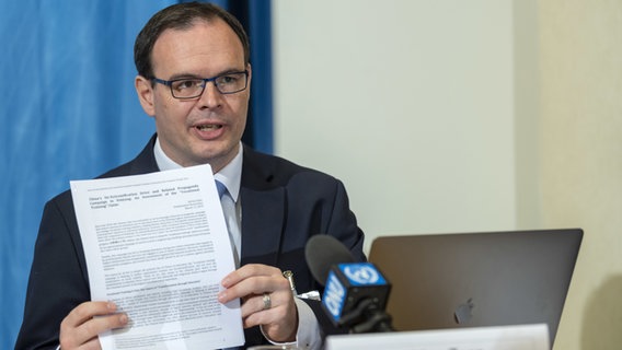 Adrian Zenz hält am Schreibtisch sitzend ein Papier hoch. Adrian Zenz hält am Schreibtisch sitzend ein Papier hoch. © dpa picture alliance Foto: Martial Trezzini