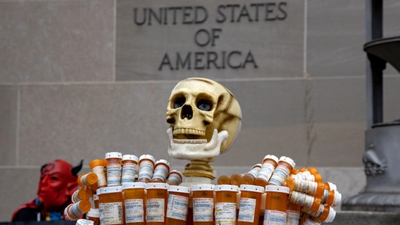 Eine Skulptur aus einem Totenschädel und leeren Medikamentendosen steht bei Protesten gegen große Pharmakonzerne vor einem US-amerikanischen Gerichtsgebäude. © picture alliance / NurPhoto | Bryan Olin Dozier Foto: Bryan Olin Dozier