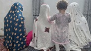 Sitzende verschleierte Mädchen (von hinten fotografiert) in einem afghanischen Wohnzimmer. © ARD 
