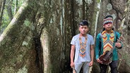 Zwei indigene Jungen vor einem Baum, um den die "Liane der Geister" wächst. © ARD Foto: Anne Herrberg