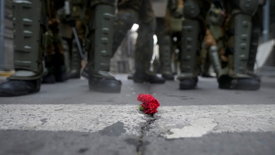 Polizisten stehen vor einer Blume, die während einer Demonstration zum 50. Jahrestag des Militärputsches von General Pinochet vor dem Präsidentenpalast La Moneda auf die Straße gelegt wurde. © picture alliance Foto: Esteban Felix