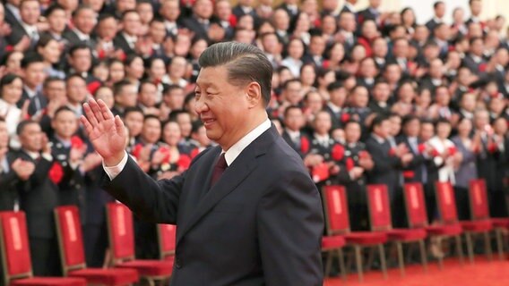 Xi Jinping hebt die Hand bei einer Veranstaltung in der großen Halle des Volkes. © dpa picture alliance Foto: Huang Jingwen