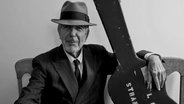 Leonard Cohen mit Hut und dem Arm auf dem Gitarrenkoffer. © picture alliance 