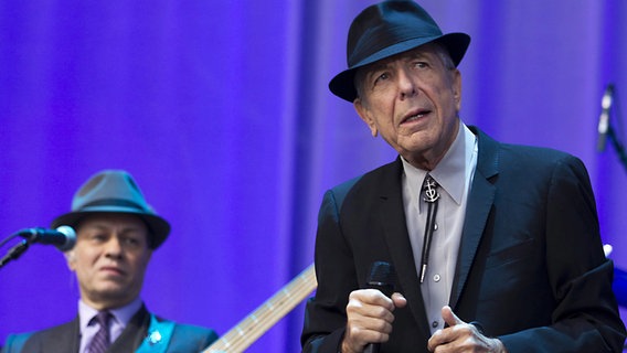 Leonard Cohen mit Mikro und Gitarrist auf der Bühne. © picture alliance Foto: Paul Bergen