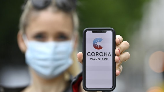 Ein Handy mit der geöffneten Corona Warn-App wird von einer Frau in die Luft gehalten. © dpa picture alliance Foto: Michael Weber