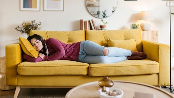 Eine junge Frau liegt zufrieden auf dem Sofa. © dpa picture alliance Foto: Westend 61 / Xavier Lorenzo