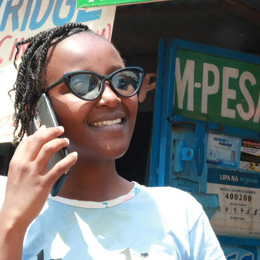 Eine Frau telefoniert mit einem Mobiltelefon in Nairobi, dahinter ein M-PESA Schriftzug. © ARD Foto: Antje Diekhans