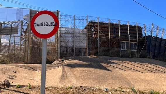 Ein meterhoher Stacheldrahtzaun mit Hinweisschild "Zona de Seguridad". © ARD Foto: Franka Welz