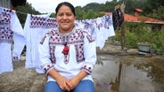 Virginia Balbuena sitzt in einer traditionellen Bluse vor weiteren Blusen. © ARD Foto: Jenny Barke