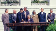 Israels Außenminister Shimon Peres (li.) unterzeichnet das historische Oslo-Abkommen (1993). Rechts von ihm Palästinenser-Präsident Jassir Arafat, links von ihm US-Präsident Bill Clinton. © picture alliance Foto: Arnie Sachs