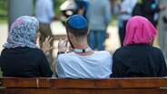 Zwei junge Muslimas mit Kopftuch und ein junger jüdischer Mann mit Kippa unterhalten sich miteinander © picture alliance Foto: Monika Skolimowska