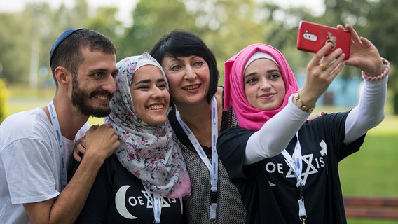 Zwei junge Muslimas mit Kopftuch und ein junger jüdischer Mann mit Kippa machen ein Selfie mit Inna Shames, Union progressiver Juden e.V. © picture alliance Foto: Monika Skolimowska