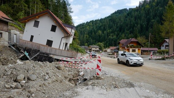 Ein Haus mit Fundament hat es aus dem Erdboden gerissen und steht schräg an einer Straße. © ARD Foto: Wolfgang Vichtl