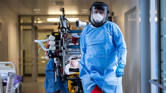 Auf einer Intensivstation liegt ein Covid-19-Erkrankter auf einer Intensiv-Trage, gezogen von einem Krankenhausmitarbeiter in Schutzkleidung. © dpa picture alliance Foto: Sebastian Gollnow