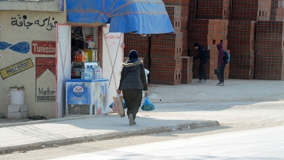 Vor einem Geschäft in Tunis geht eine Frau mit Brot und Lebensmitteln in ihren Tüten. © picture alliance / ZUMAPRESS Foto: Chokri Mahjoub