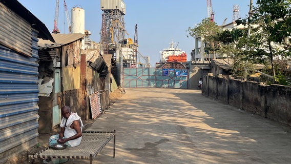 Der Eingang einer indischen Werft, ein Arbeiter sitzt davor. © NDR Foto: Peter Hornung