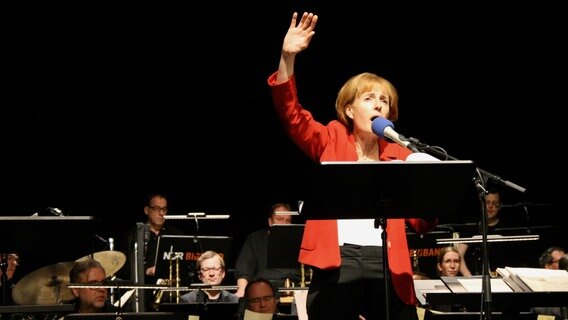 Antonia von Romatowski als Angie Merkel mit der NDR Bigband auf der Bühne der Burg in Seevetal am 28.11.2021. © NDR Foto: Jenny von Gagern