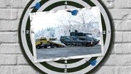 Eine Bildmontage zeigt eine Dartscheibe. Darauf ist eine Postkarte zu sehen. Sie zeigt einen Abschleppwagen, der einen Puma-Panzer abschleppt. © dpa Foto: Michael Hutter / Philipp Schulze