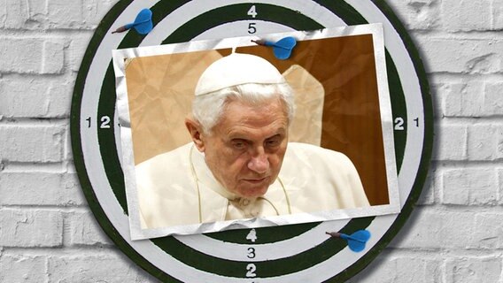 Eine Bildmontage zeigt eine Dartscheibe. Darauf ist eine Postkarte zu sehen. Sie zeigt den ehemaligen Papst Benedikt. © imago images / ZUMA Press Foto: imago images / ZUMA Press