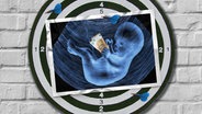 Eine Bildmontage zeigt eine Dartscheibe. Darauf ist eine Postkarte zu sehen. Sie zeigt das Ultraschallbild eines ungeborenen Kindes. Das Kind hält zwei 50-Euro-Scheine in der Hand. © Imago Images Foto: Imago Images
