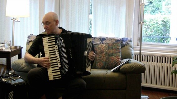 Guy Klucevsek sitzt auf einem Sofa und spielt das Akkordeon © Everett Collection 