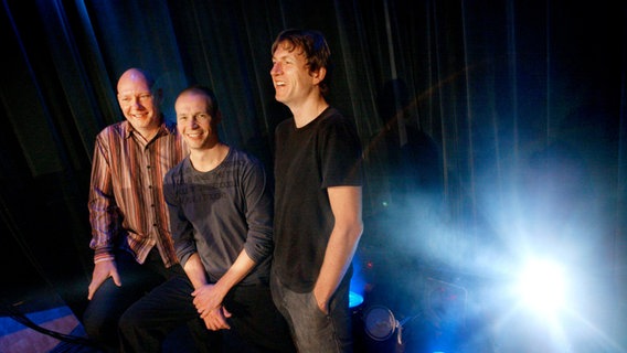 Drei Männer posieren auf einer Bühne. © Jessica Gow Foto: Jessica Gow