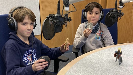 Zwei Jungen sitzen vor Mikrofonen und halten Spielzeug in der Hand © NDR/Schlage 