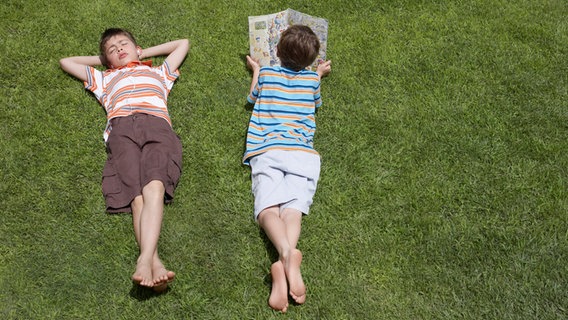 Zwei Kinder liegen auf einer Wiese und lesen © IMAGO / YAY Images 